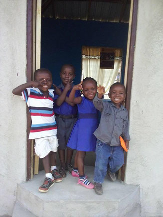 Kids in a Door Frame – 4 People Four cheerful kids stand in front of a door, smiling and posing. The boys wear striped and solid shirts, the girl has a blue dress.
