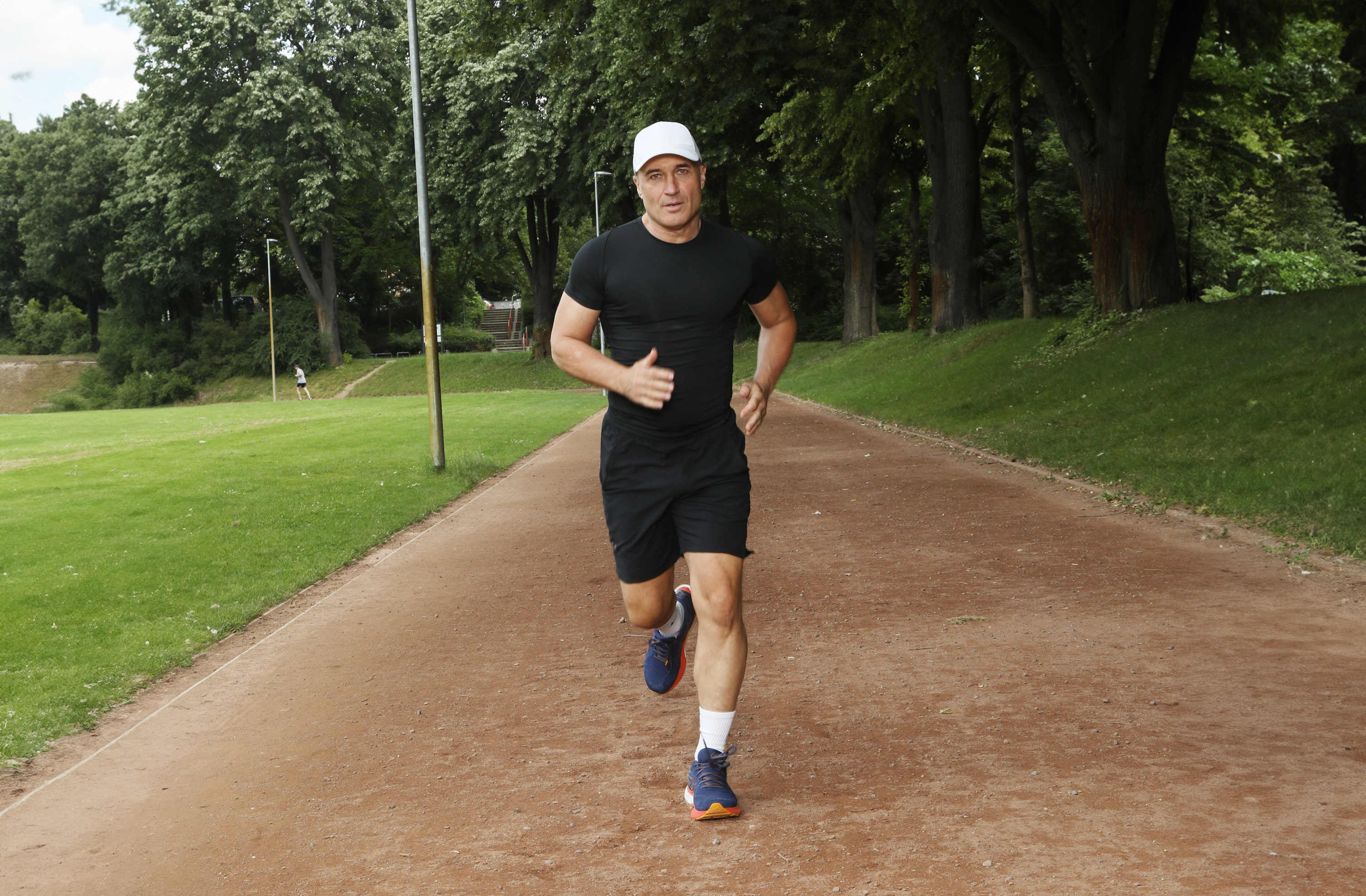 Running Shoes Men – Sporty 10 km Models Man jogging on a forest path, wearing black sportswear and blue running shoes.