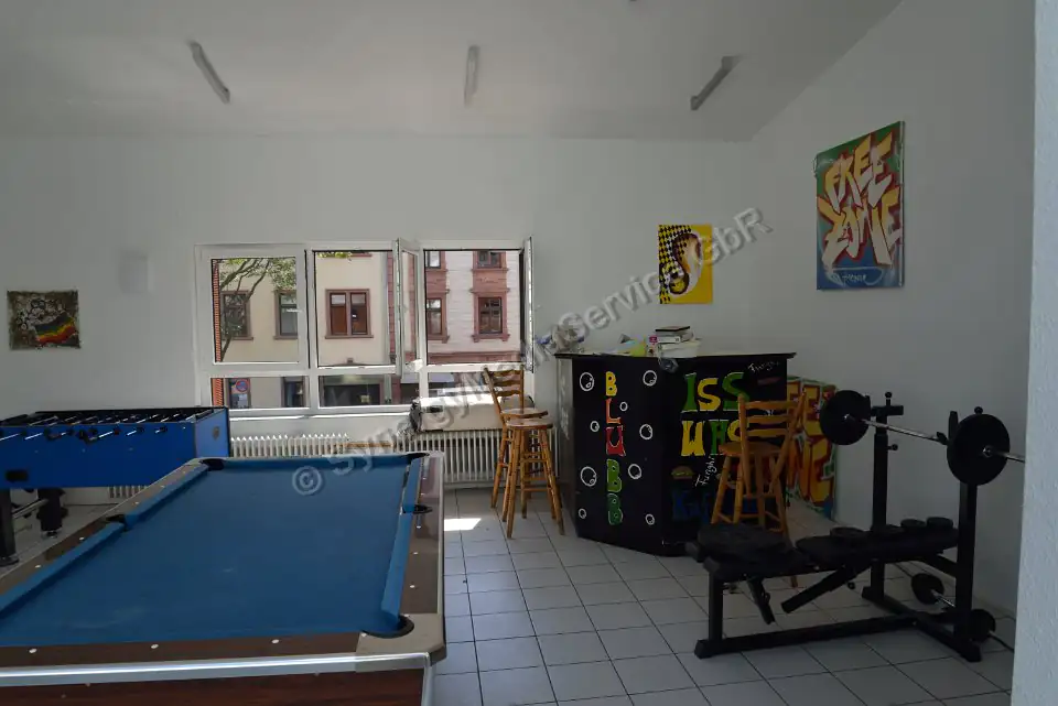 Recreation Room with Pool Table and Gym Equipment Bright recreation room featuring a pool table, foosball, gym equipment, and a bar, with large windows.