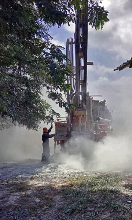 Drilling Machine – On-Site Water Drilling Worker operates a drilling machine in a dusty environment with trees in the background.